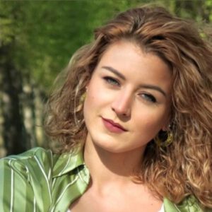 Love Guide Lara steht vor einem Wald und zeigt ein leicht lächelndes Gesicht